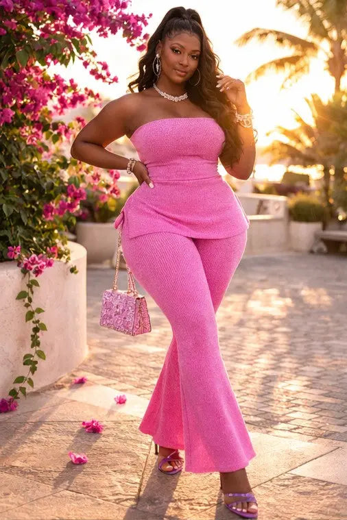 Woman in a pink outfit standing outdoors with flowers and a sunset in the background