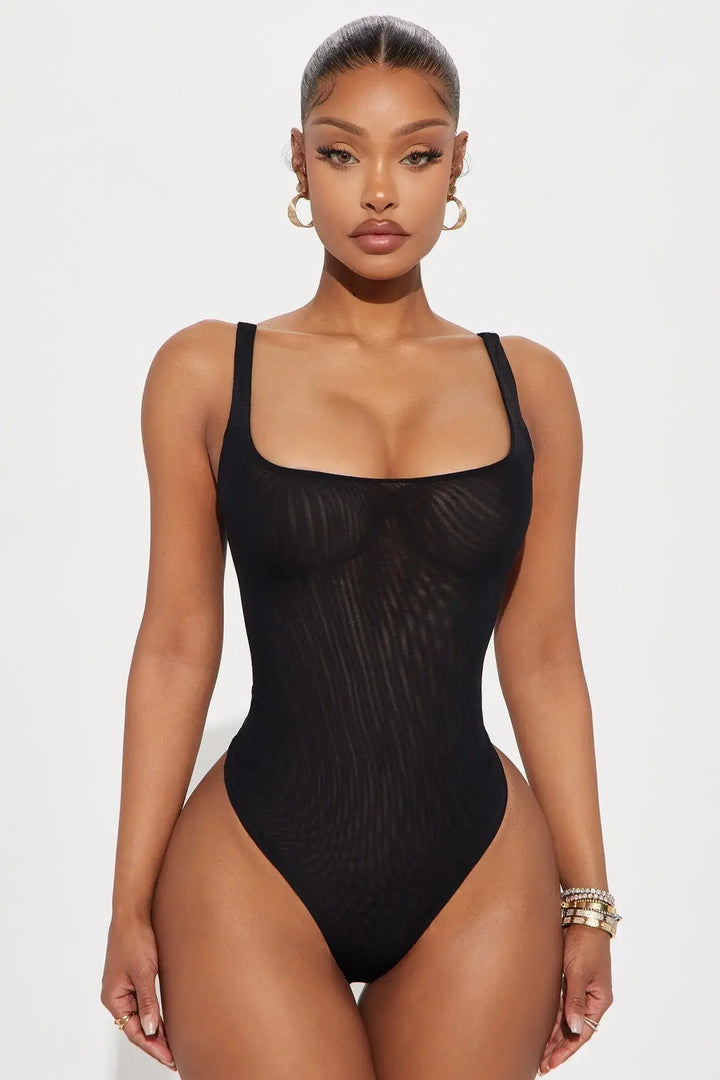 Black mesh bodysuit with square neckline styled with denim mini skirt and silver heels on model on white background