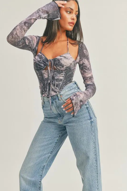 Woman wearing multicolor watertone corset mesh top with long mesh sleeves and blue jeans